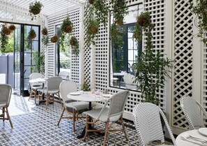Een terras met rieten meubels, hangplanten en een patroonvloer.