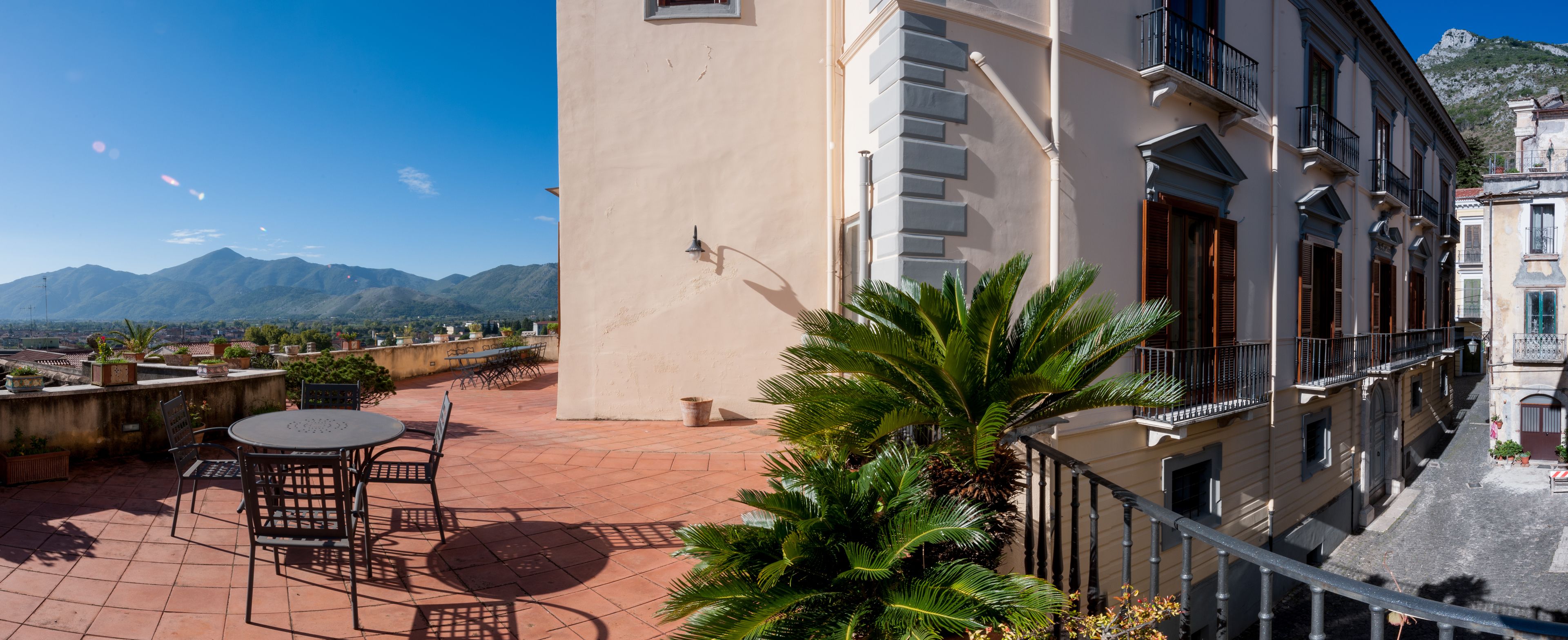 Una terraza con mesa y sillas, una palmera y vistas a las montañas.
