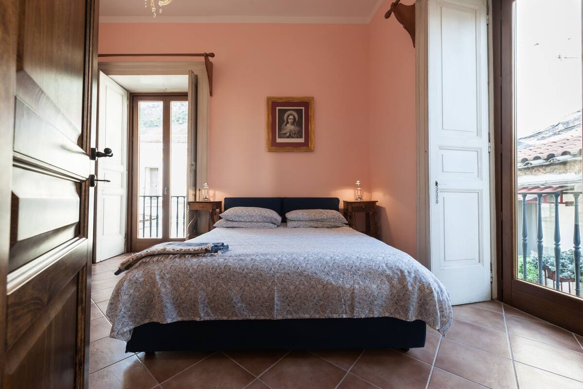 A bedroom with a bed, a nightstand, a framed picture on the wall, and a view through an open door.