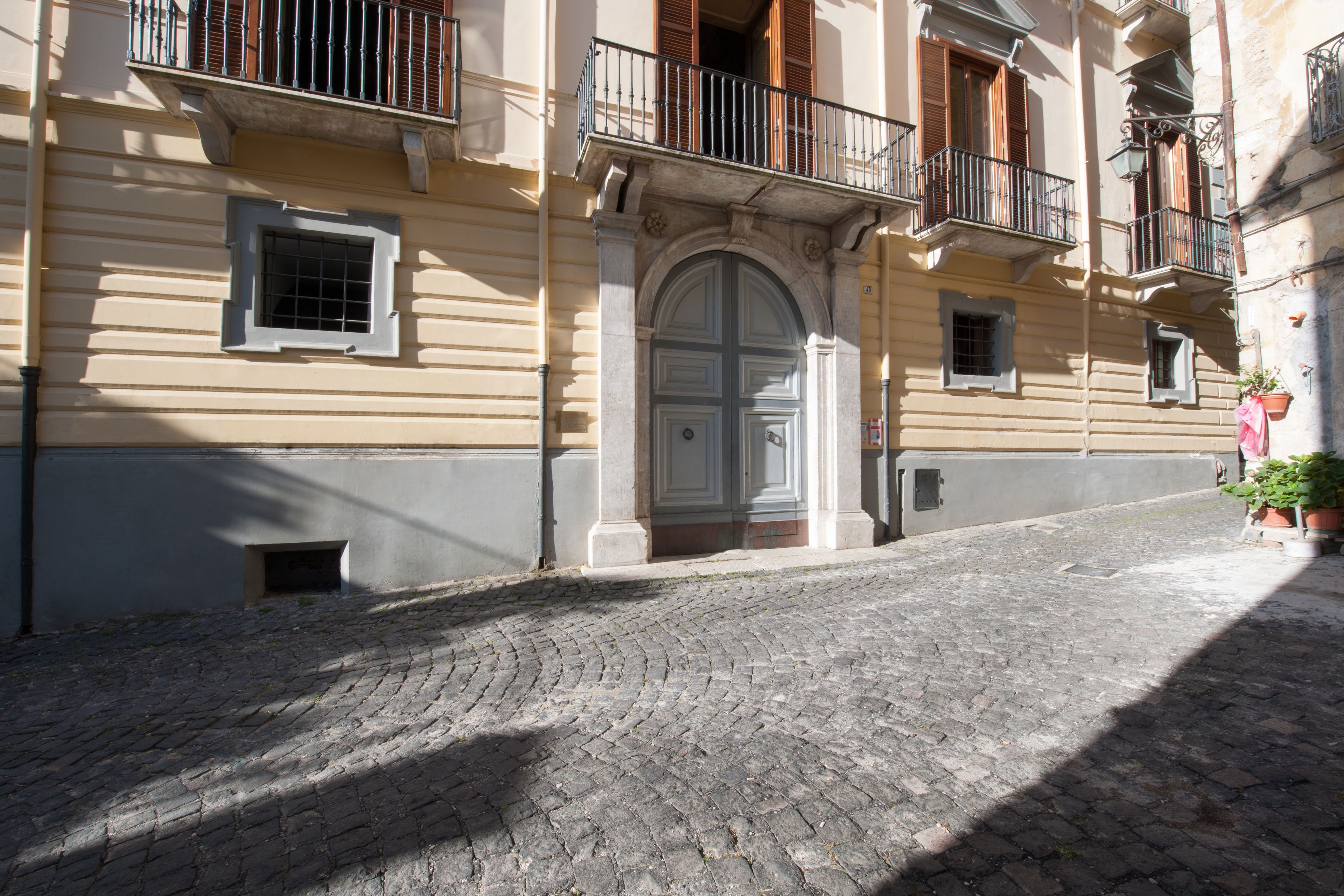 Una calle adoquinada con un edificio que presenta una gran entrada en arco, ventanas pequeñas y balcones con barandillas.