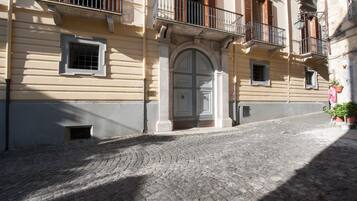Una calle adoquinada con un edificio que presenta una gran entrada en arco, ventanas pequeñas y balcones con barandillas.