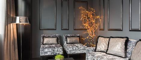 Una sala de estar moderna con una pared gris oscuro, tres cuadros enmarcados, un sofá, dos sillones, una mesa de centro con plantas y una lámpara de pie.