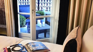 A hotel room with a bed, a window with a view of a balcony, and a magazine on the bed. - Hôtel Les Jardins de La Villa (Paris)