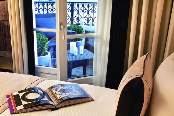 Una habitación de hotel con una cama, una ventana que ofrece vista a un balcón y una revista sobre la cama.