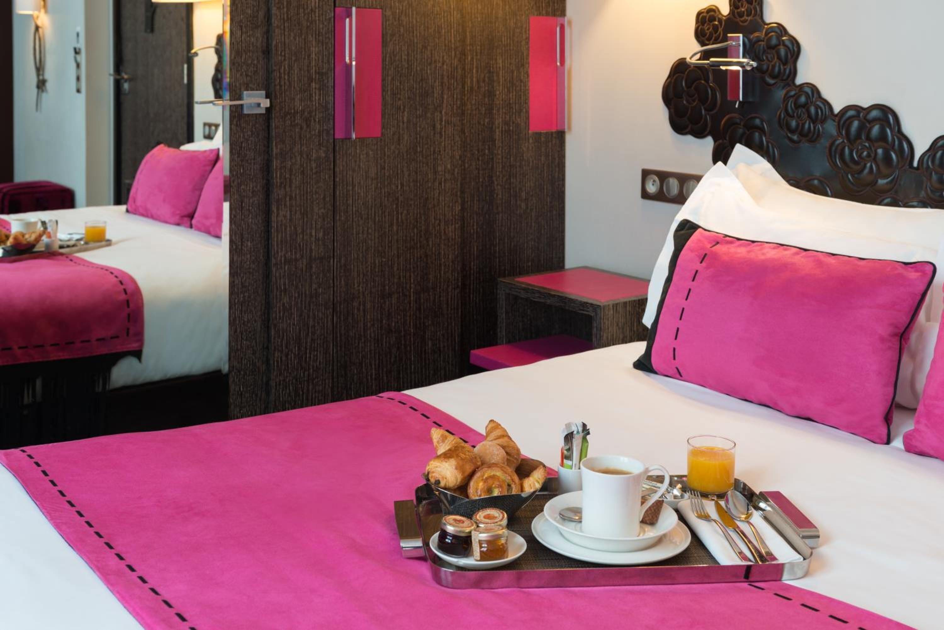 Une chambre d’hôtel avec un lit, une table de chevet et un plateau contenant des articles pour le petit-déjeuner, notamment des croissants, du café et du jus d’orange.