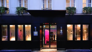A building facade with a dark entrance, large windows with frosted glass, and decorative plants on the upper level. - Hôtel Les Jardins de La Villa (Paris)