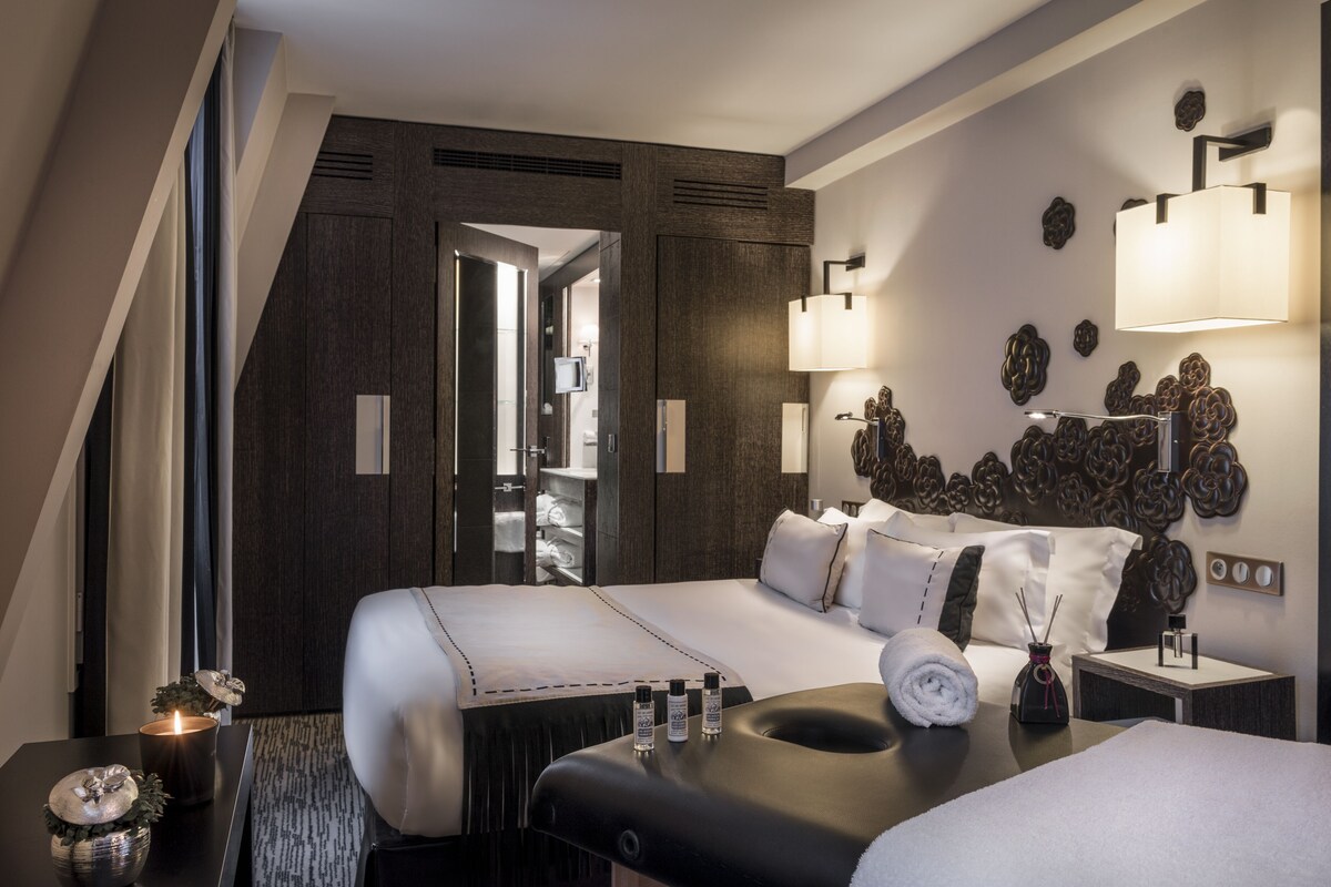 A modern hotel room with a large bed, a separate seating area, and a wall-mounted lamp.