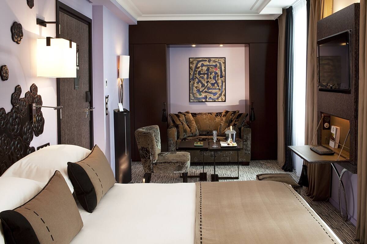 A hotel room with a large bed, a sofa, a small table, and a TV.