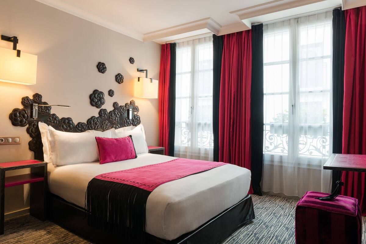 A hotel room with a large bed, a nightstand, a desk, and a window with curtains.