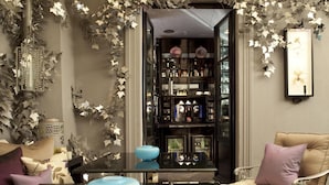 A room with a glass coffee table, a sofa with cushions, and a wall-mounted shelf with various items. - Hôtel Les Jardins de La Villa (Paris)