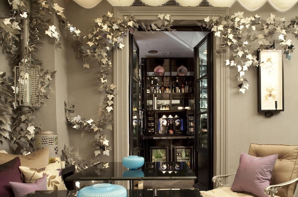 A room with a glass coffee table, a sofa with cushions, and a wall-mounted shelf with various items.