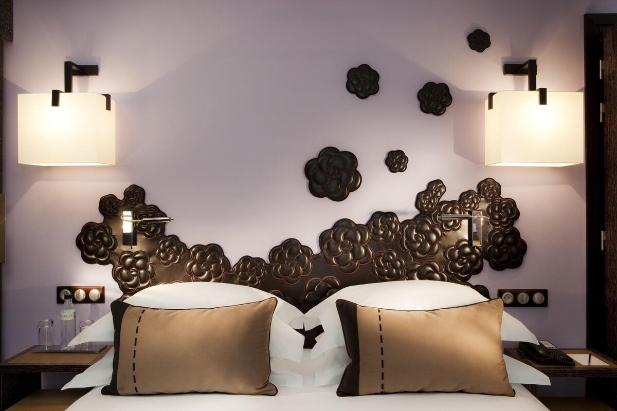 A hotel room with a large bed, two bedside lamps, a decorative wall headboard, and a small table with a lamp.