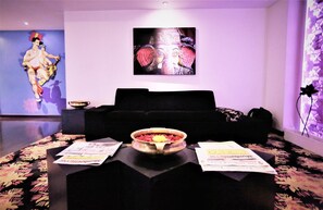 A room with a black sofa, a table with a bowl of food, and a poster on the wall. - The Beatle (Mumbai)