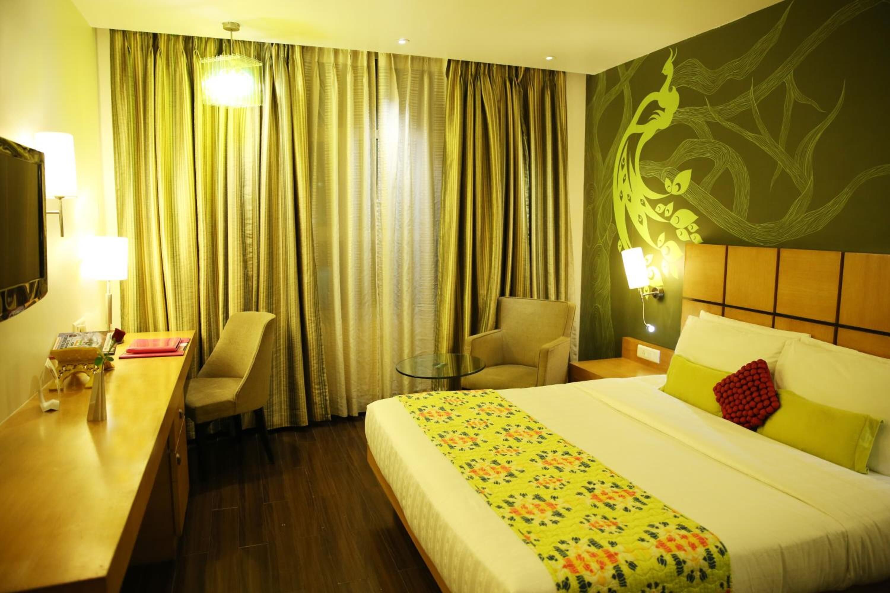 Habitación de hotel con cama, escritorio, silla, una mesita y televisor.