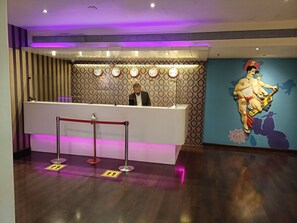 A reception desk with a patterned wall, clocks indicating different cities, and a mural of a figure on a scooter. - The Beatle (Mumbai)