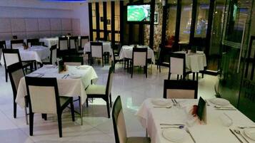 Ein Restaurant mit mehreren gedeckten Tischen, einem Fernseher im Hintergrund und Blick auf die Stadt durch große Fenster.