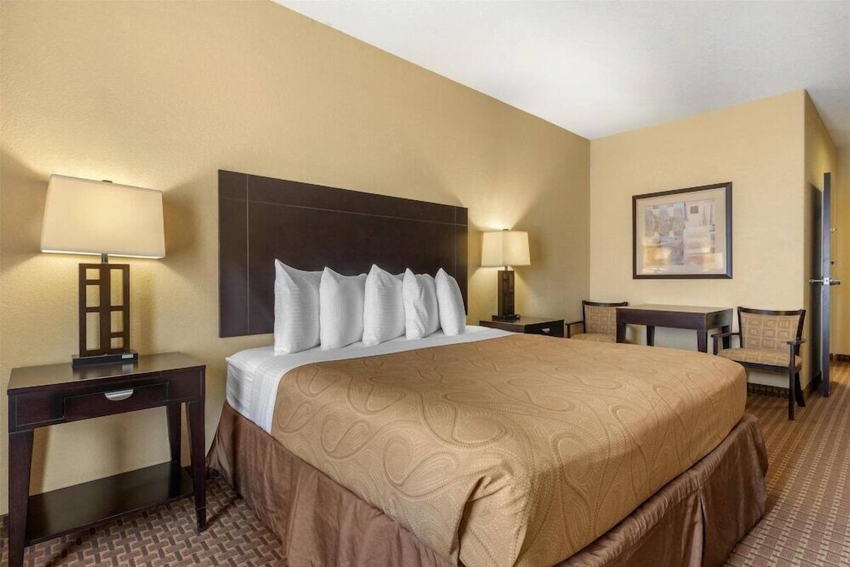 A hotel room with a large bed, two bedside tables with lamps, a desk with a chair, and a framed picture on the wall.