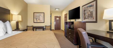 A hotel room with a large bed, a desk, a chair, a television, and artwork on the walls.