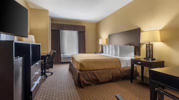 A hotel room with a bed, desk, chair, TV, and a window with curtains.
