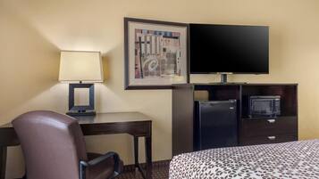 Une chambre d’hôtel équipée d’un lit, d’un bureau, d’une chaise, d’une télévision, d’un four à micro-ondes et d’une œuvre d’art encadrée accrochée au mur.