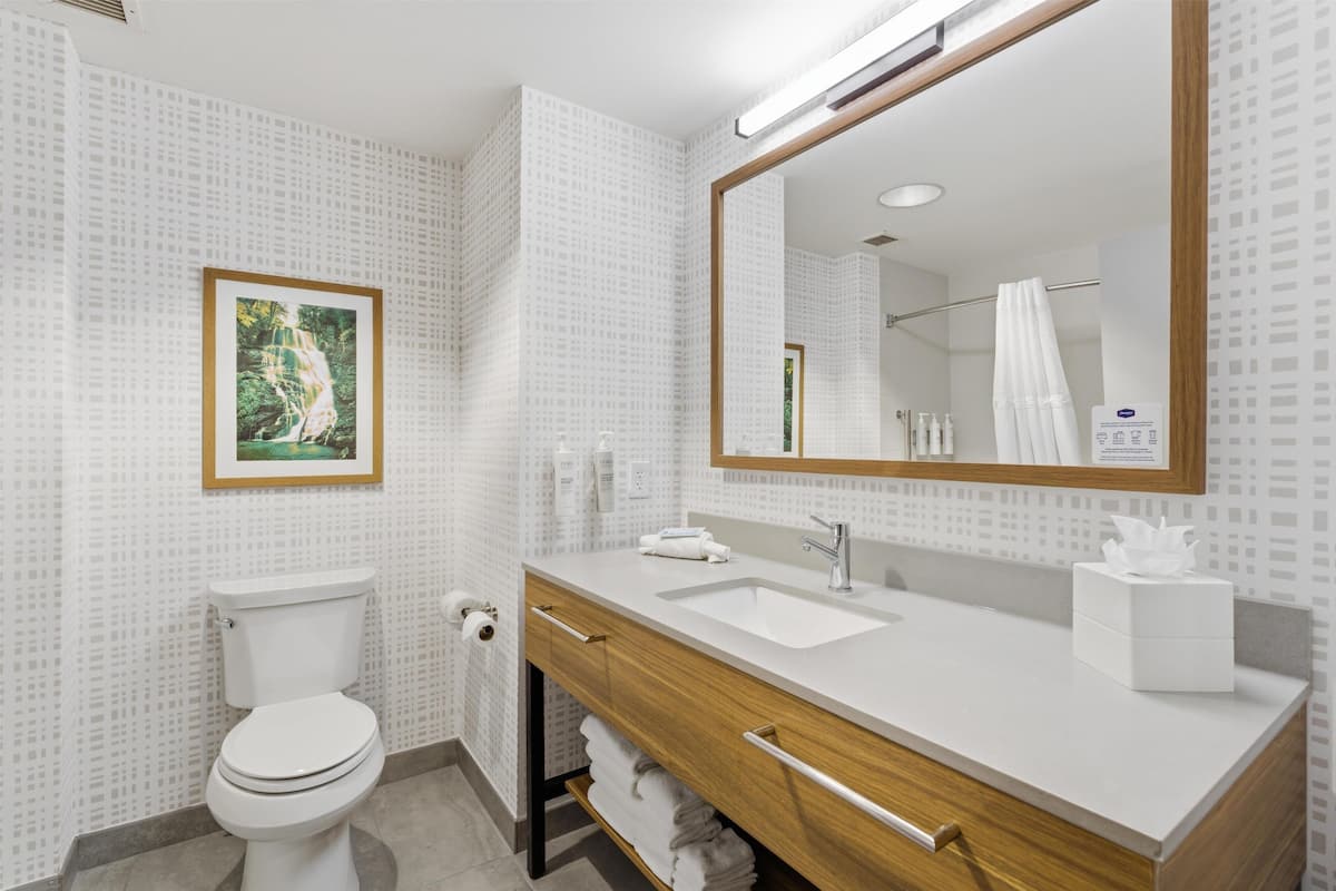 A modern bathroom with a toilet, sink, vanity, and a large mirror.