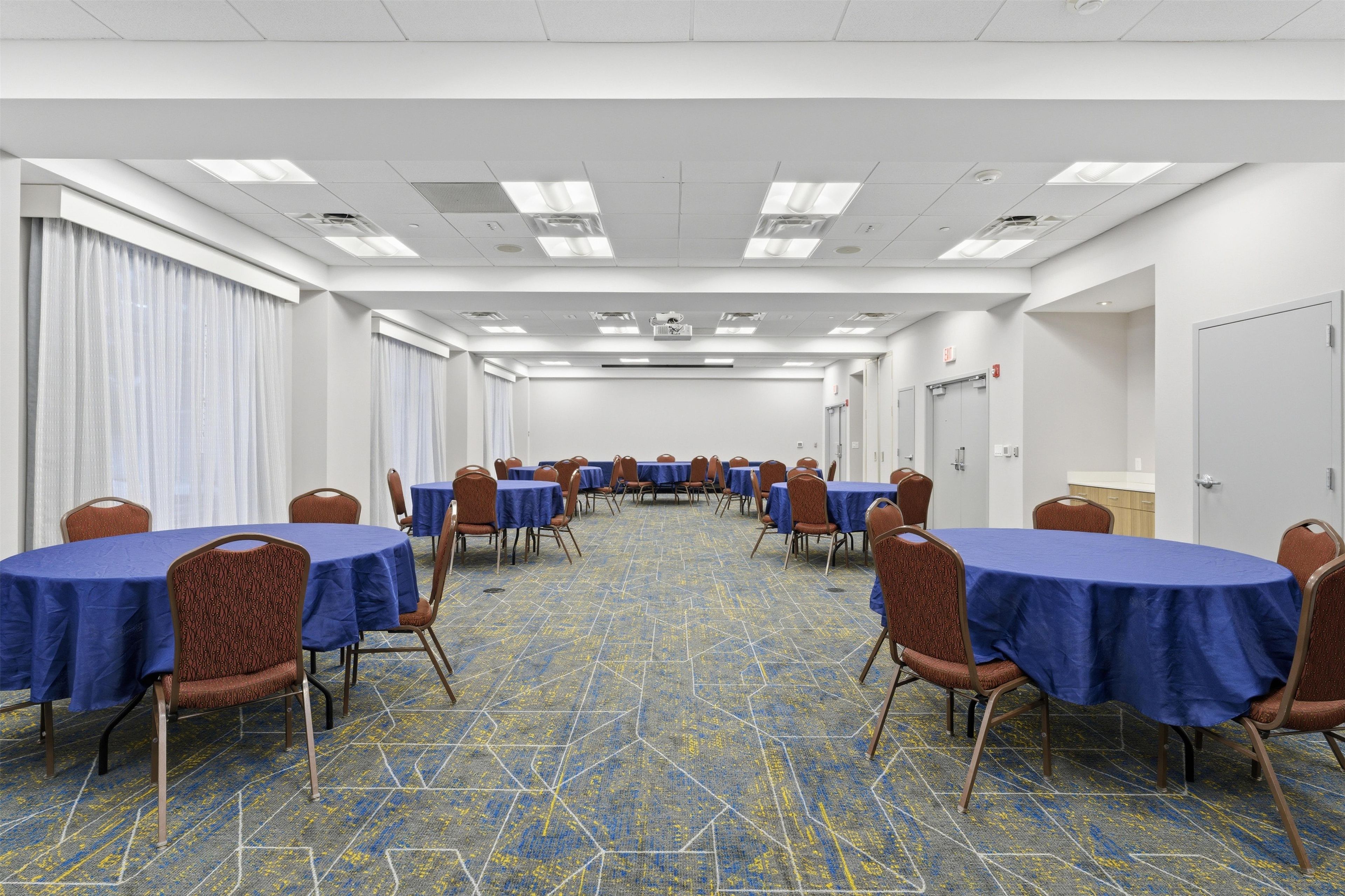 A conference room with tables and chairs, a patterned carpet, and a white ceiling with lights.