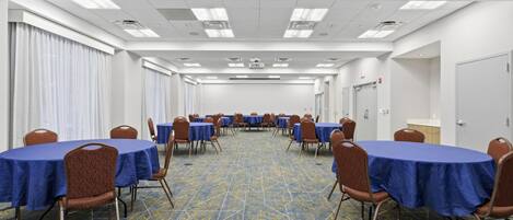 A conference room with tables and chairs, a patterned carpet, and a white ceiling with lights.