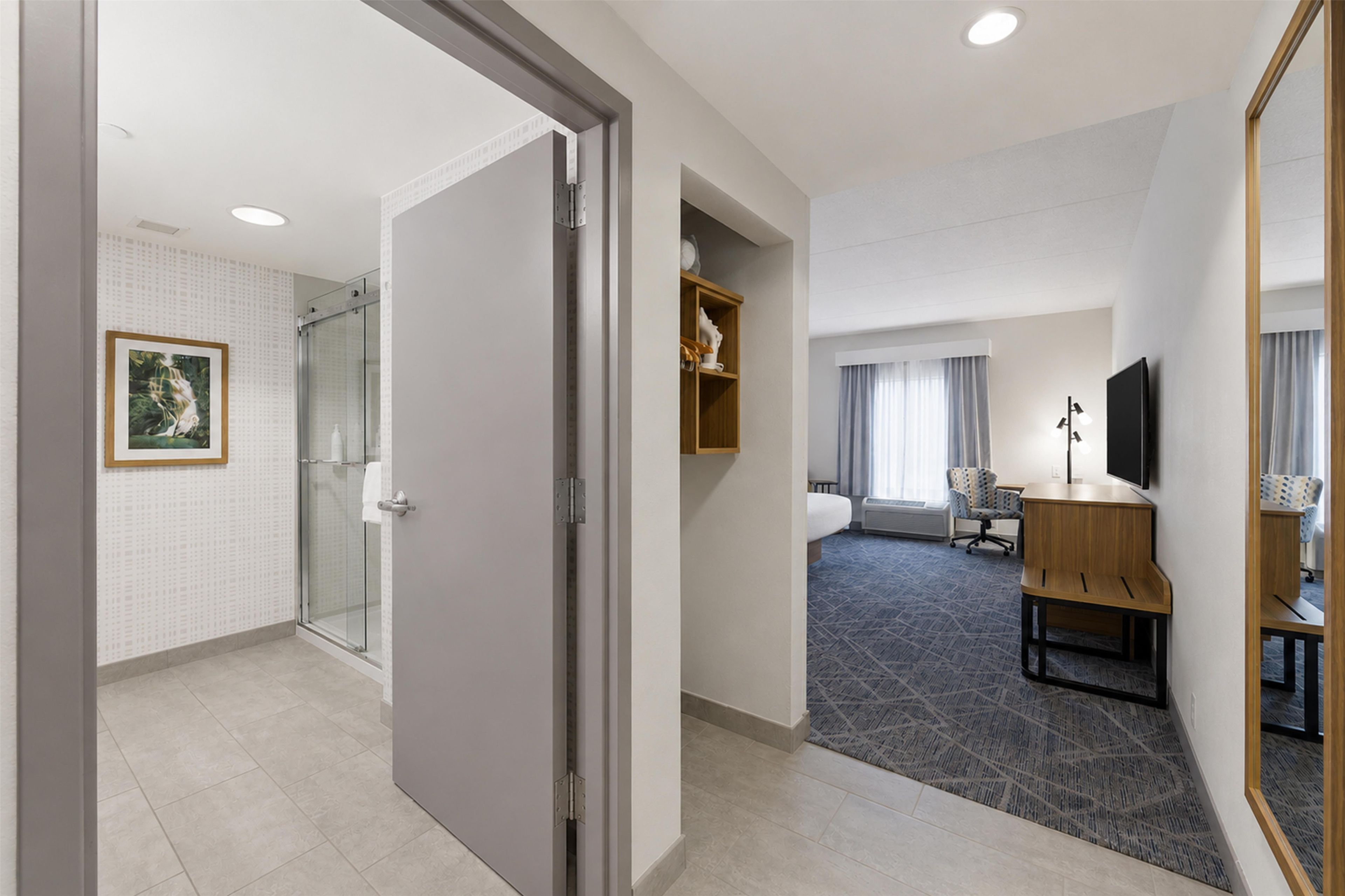 Habitación de hotel con ducha, cama, escritorio, silla, televisor y ventana con cortinas.