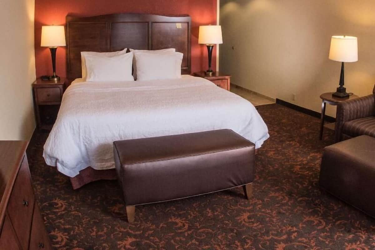 A hotel room with a large bed, two bedside tables with lamps, a brown leather bench, and a patterned carpet.