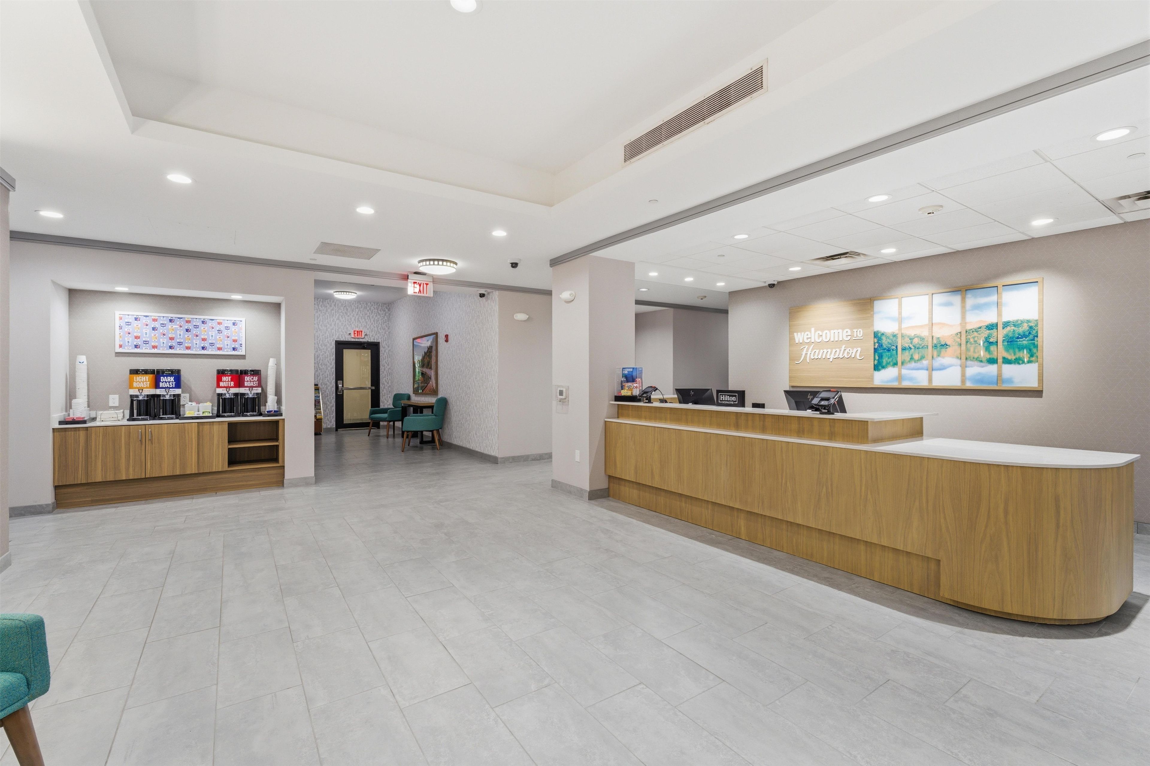A hotel reception area with a reception desk, a coffee station, and a seating area with chairs.