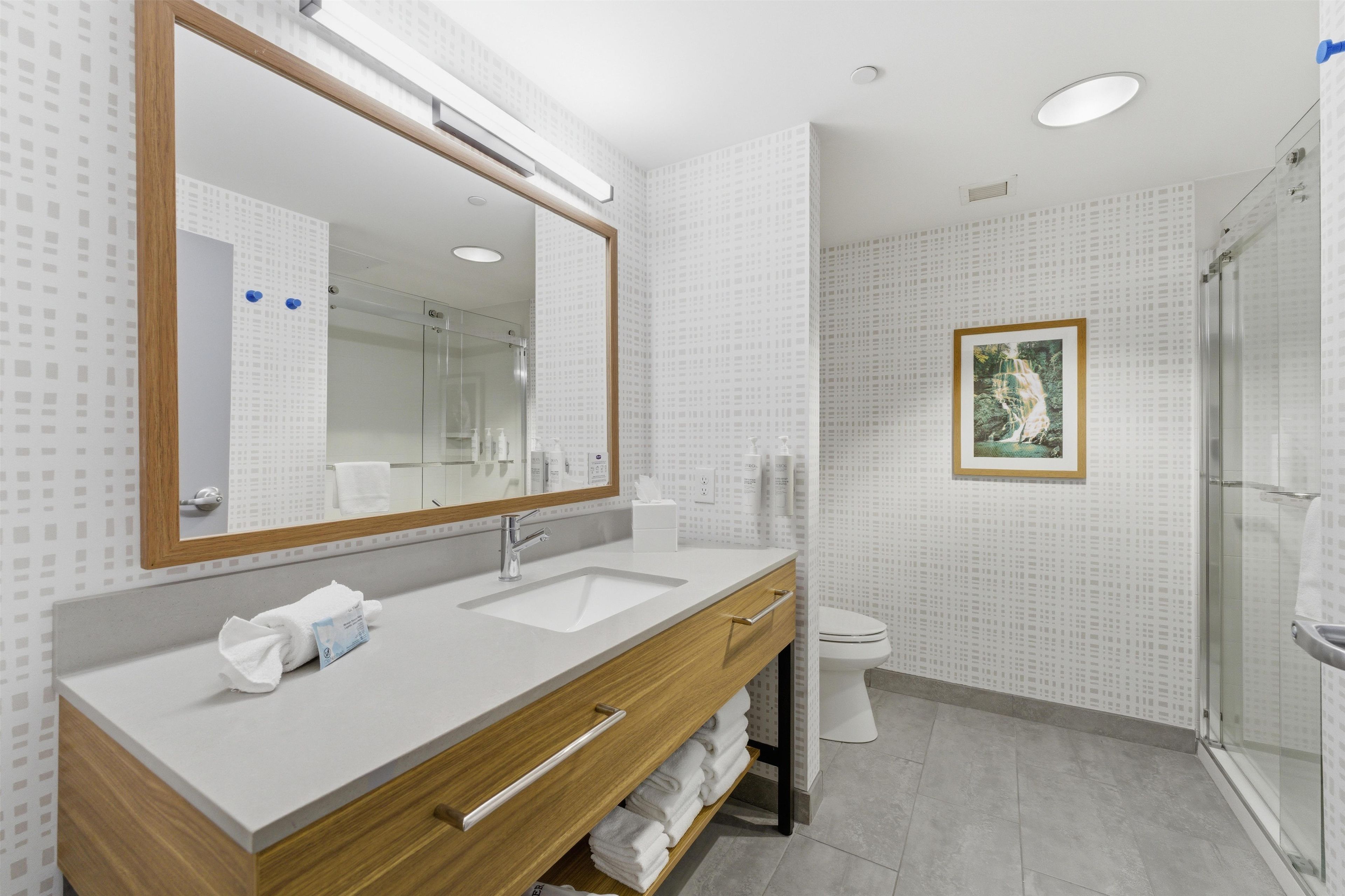 Uma casa de banho moderna com um espelho grande, duas pias, uma sanita e um chuveiro.