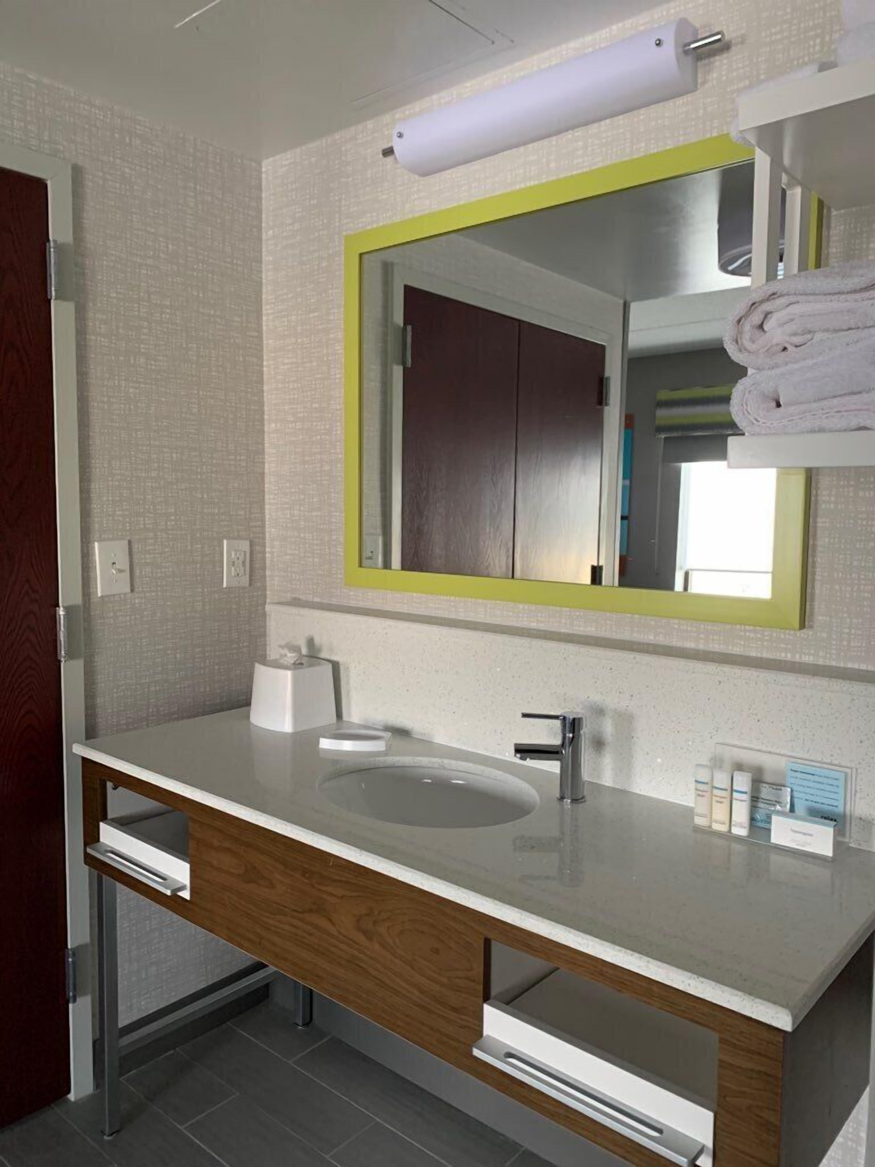 Une salle de bain moderne avec un lavabo blanc, un miroir avec un cadre jaune et un porte-serviettes.
