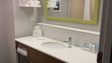 A modern bathroom with a white sink, a mirror with a green frame, and neatly stacked towels on a shelf.