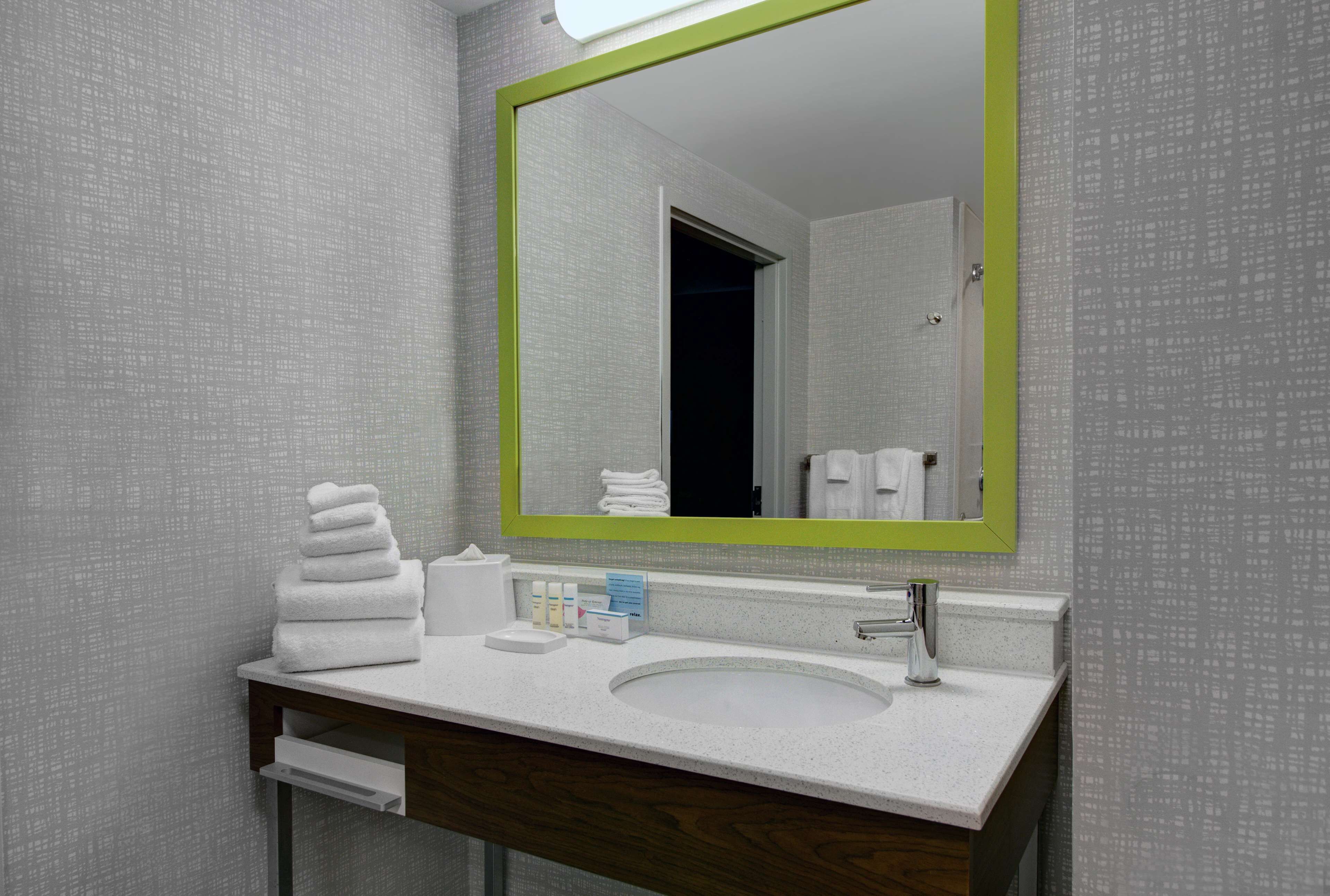 A modern bathroom with a white sink, a mirror with a green frame, and neatly stacked towels.