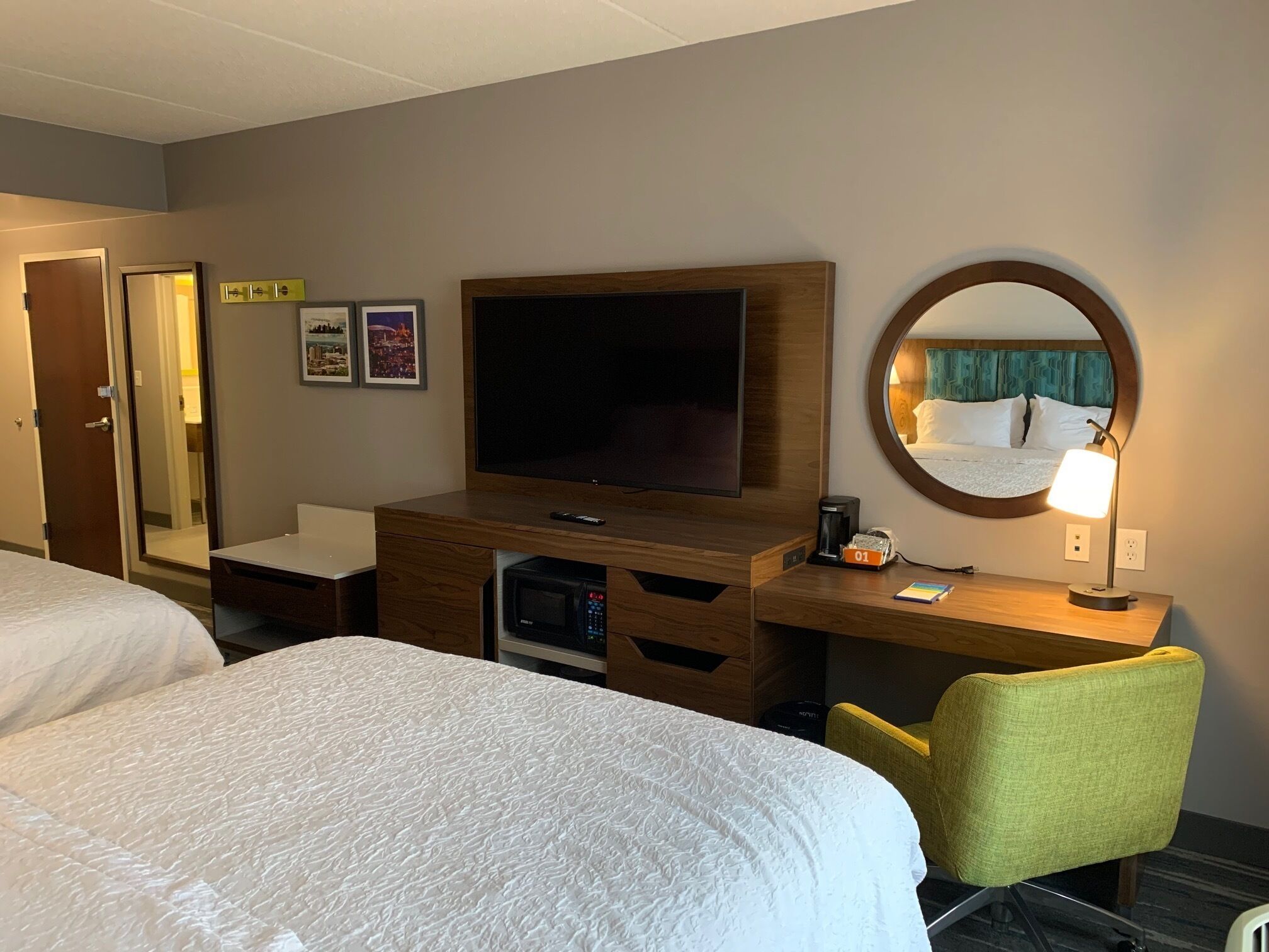 Ett hotellrum med två sängar, en TV, ett skrivbord med en lampa, en mikrovågsugn och en spegel.
