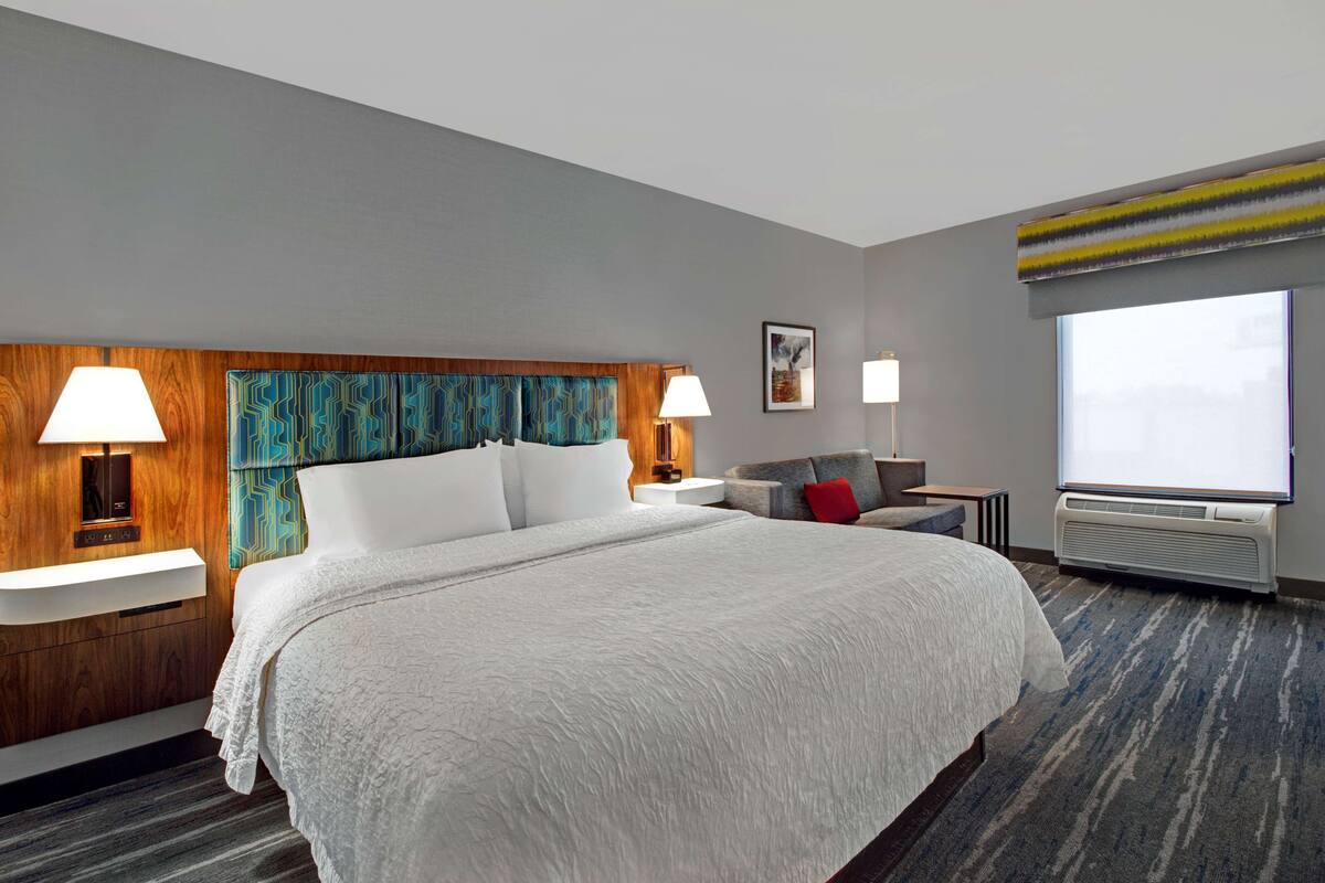 A hotel room with a large bed, two bedside lamps, a TV, and a window with a view.
