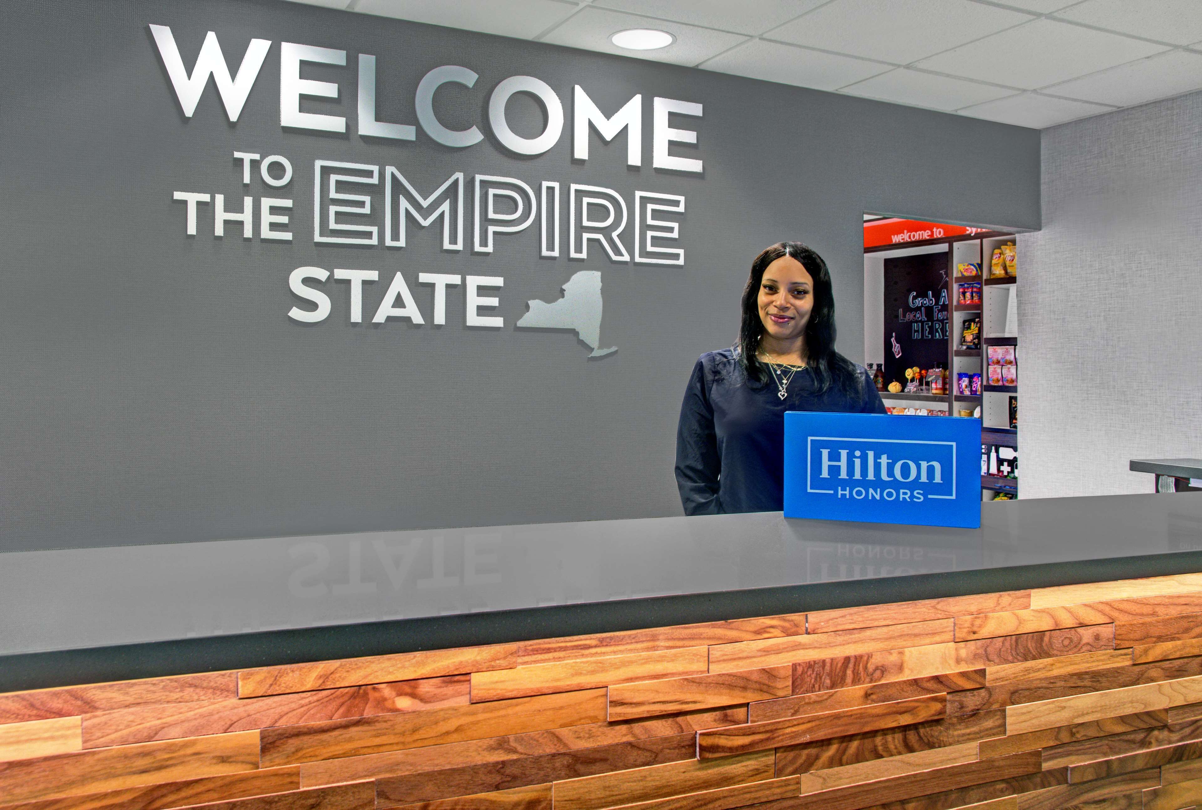 Un comptoir d’accueil avec une pancarte indiquant « BIENVENUE À L’EMPIRE STATE » et une autre pancarte « Hilton Honors ».