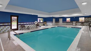 Una piscina interior con paredes azules y blancas, suelo de baldosas y una puerta que da al exterior.