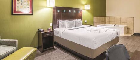 Una habitación de hotel con cama, mesita de noche, lámpara, silla, banco y bañera.