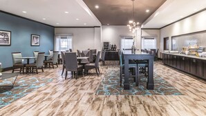A modern dining area with a central table, surrounding chairs, and a buffet counter. - La Quinta Inn & Suites by Wyndham Dallas Grand Prairie South (Grand Prairie)