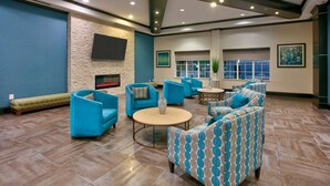 A spacious lobby with blue sofas, a round coffee table, and a flat-screen TV mounted on the wall. - La Quinta Inn & Suites by Wyndham Dallas Grand Prairie South (Grand Prairie)