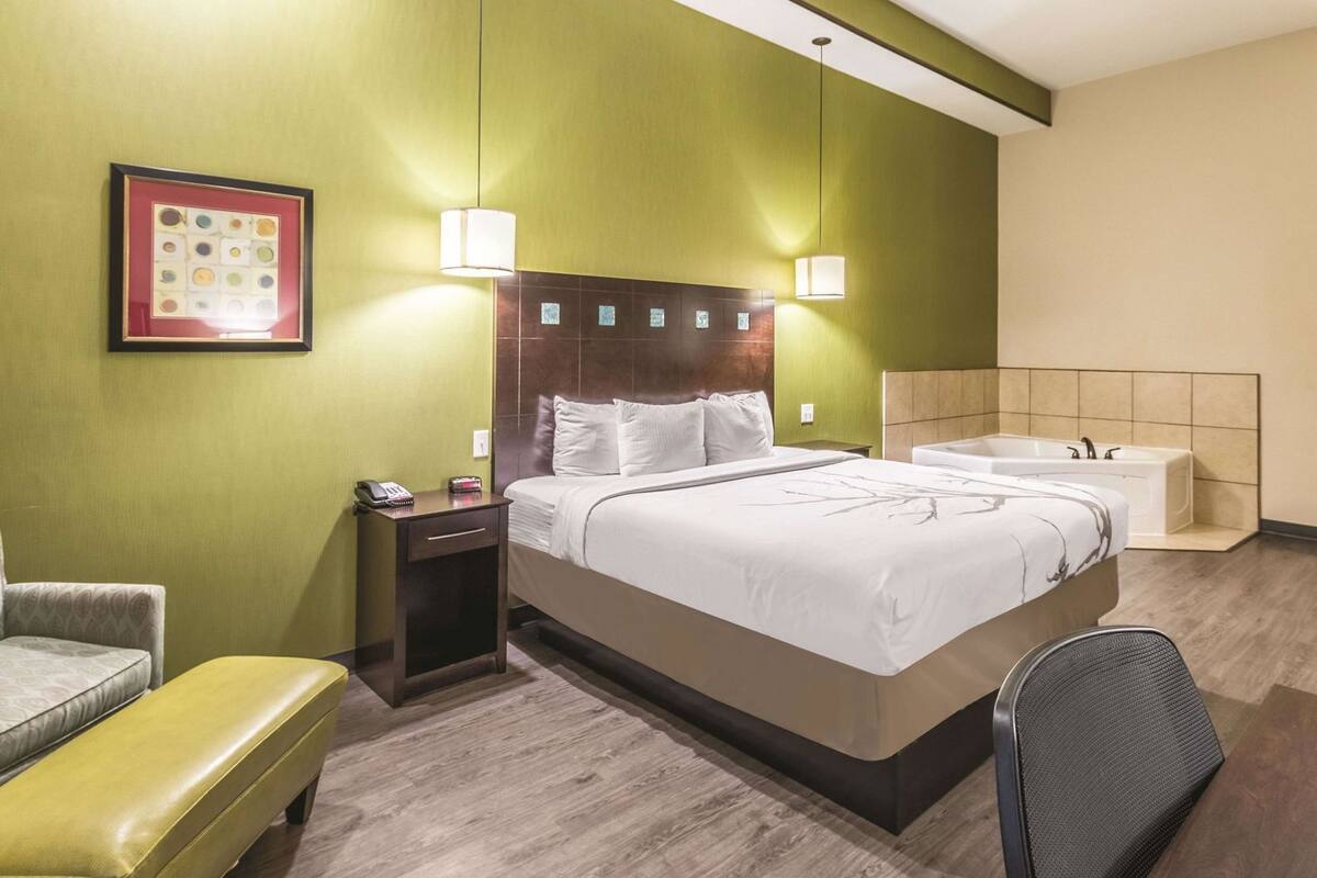 Hotellihuone, jossa on sänky, yöpöytä, lamppu, tuoli, penkki ja kylpyamme.