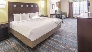 A hotel room with a large bed, a desk with a chair, a small table, and a sofa. There is a window with curtains and a view of the outside. - La Quinta Inn & Suites by Wyndham Dallas Grand Prairie South (Grand Prairie)
