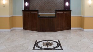 A reception desk with a patterned wallpaper backdrop, two wall-mounted lights, and a decorative floor design. - Super 8 by Wyndham Rosenberg TX (Rosenberg)