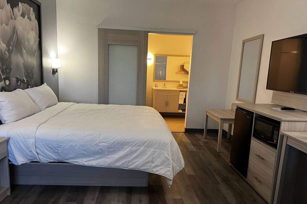 Quarto com cama, mesa de cabeceira, televisão e vista para o banheiro.