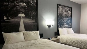 A hotel room with two beds, a nightstand, a wall-mounted light, and a large framed picture of a tree-lined pathway. - Super 8 by Wyndham Rosenberg TX (Rosenberg)