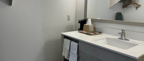 A modern bathroom with a white sink, a mirror, a towel rack, and a coffee maker.