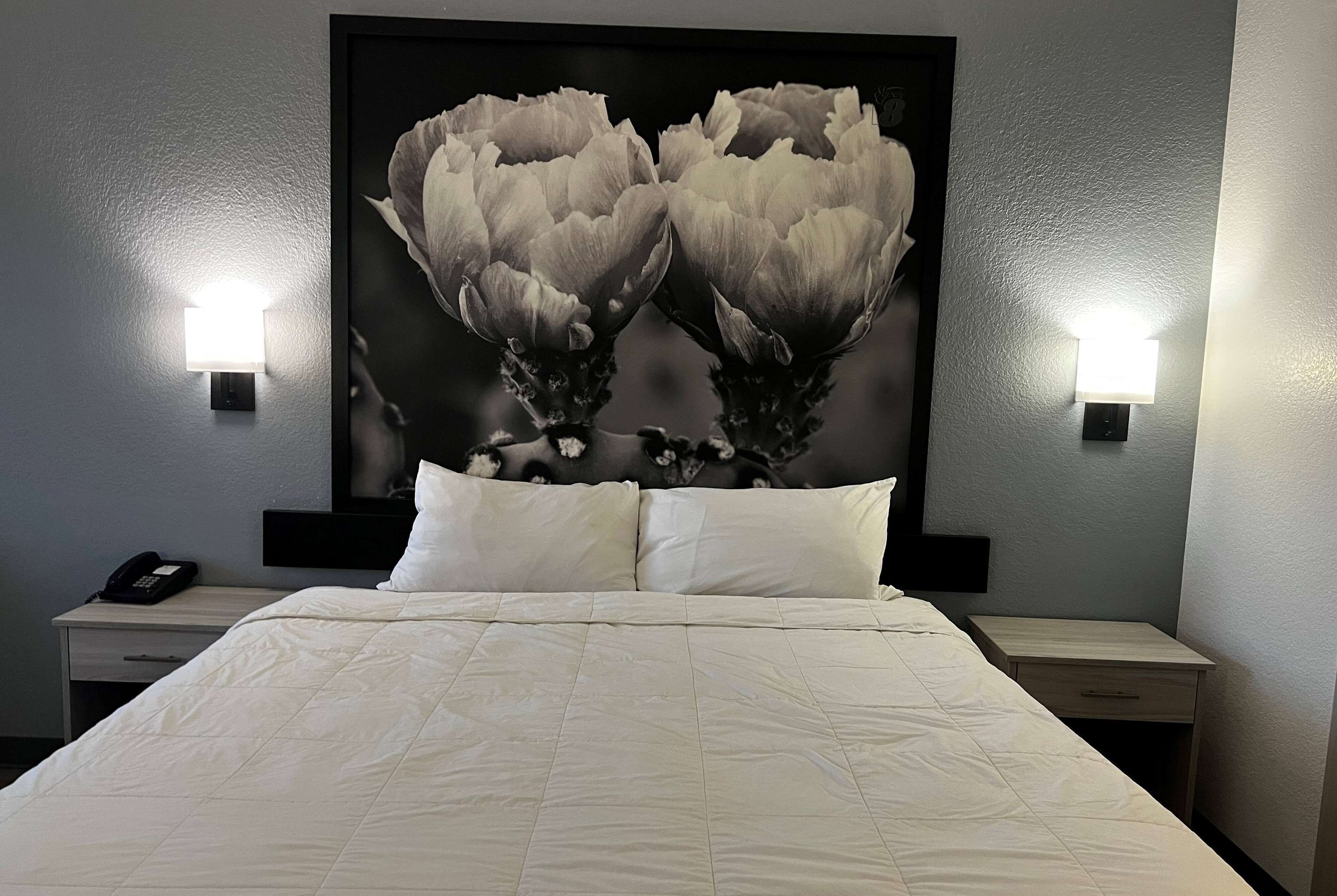 A neatly made bed with white bedding, two bedside tables with lamps, and a large floral artwork on the wall.