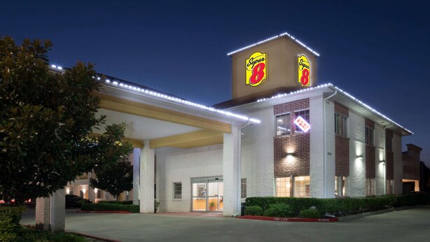 A Super 8 hotel with a prominent 'Super 8' sign, a well-lit entrance, and a parking area. - Super 8 by Wyndham Rosenberg TX (Rosenberg)
