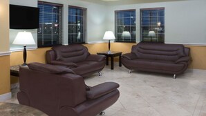 A living room with two brown leather sofas, a flat-screen TV mounted on the wall, and two lamps on side tables. - Super 8 by Wyndham Rosenberg TX (Rosenberg)